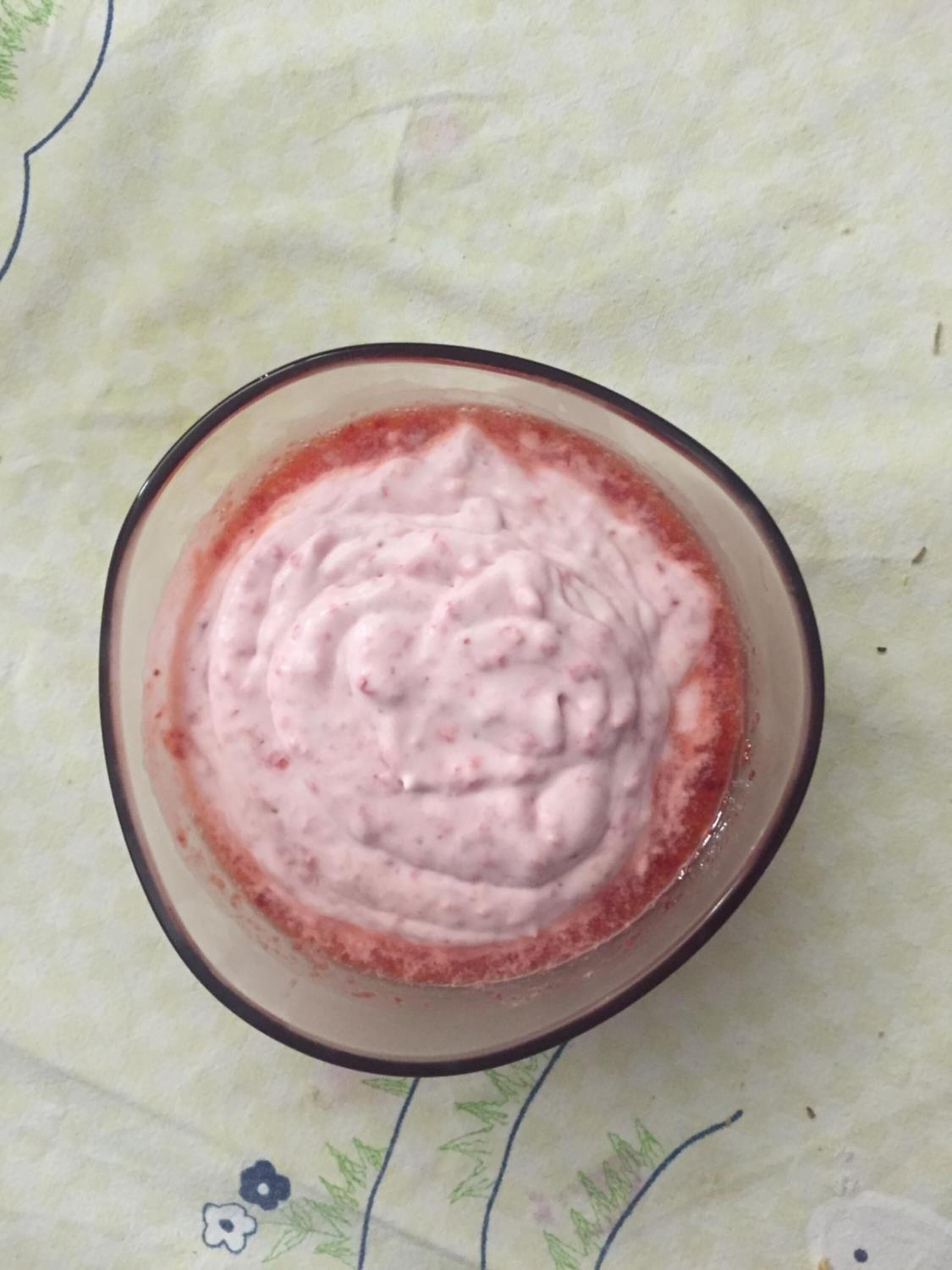 A bowl of pink smoothie on a table with a floral tablecloth.