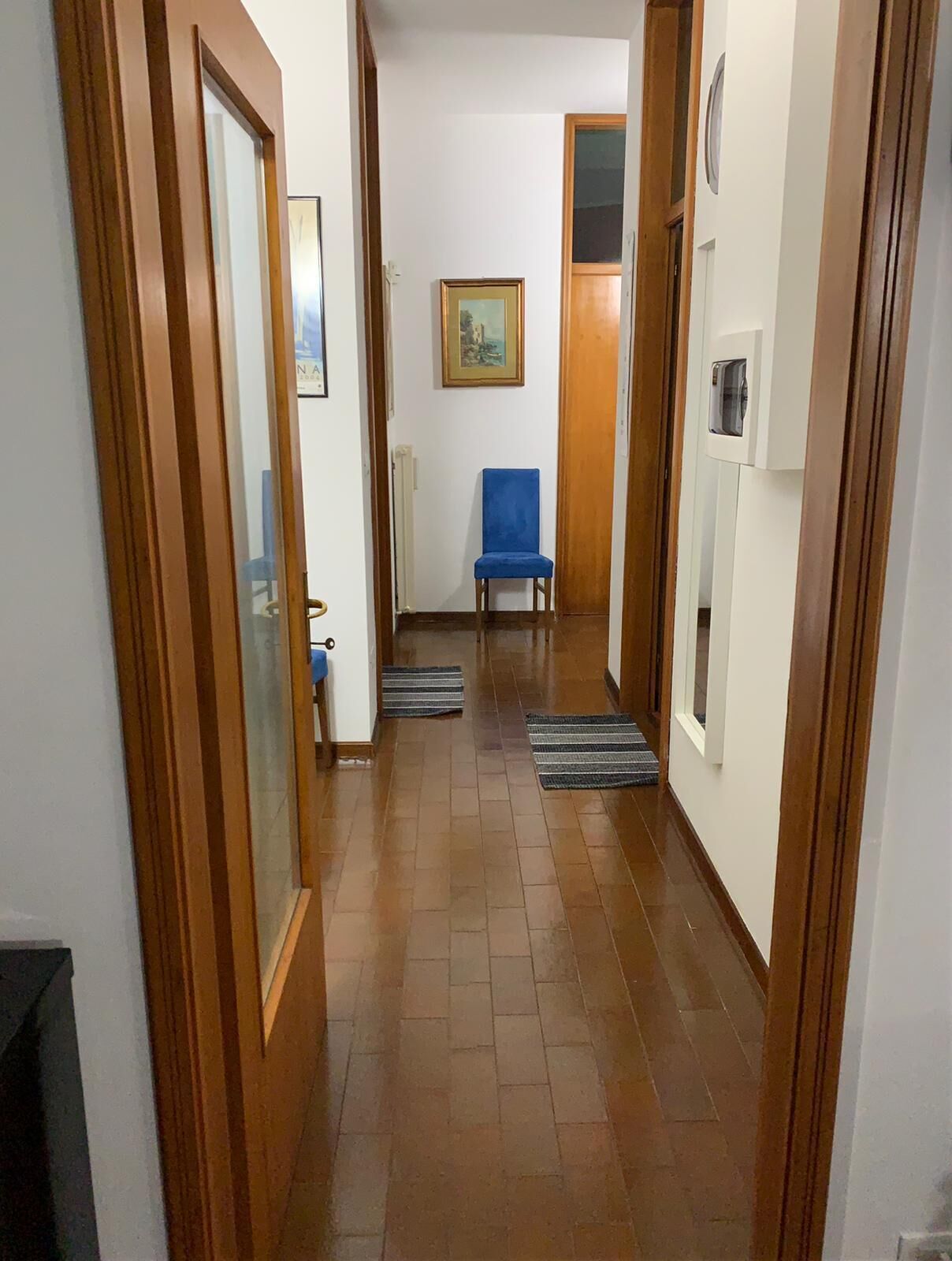 Un pasillo con puertas de madera, una silla azul, un radiador y un cuadro enmarcado en la pared.