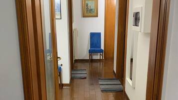 Un pasillo con puertas de madera, una silla azul, un radiador y un cuadro enmarcado en la pared.