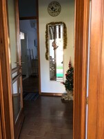 Un pasillo con puerta de madera, un espejo, un pequeño árbol de Navidad y un reloj en la pared.