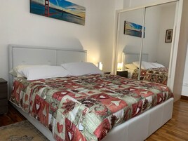 Un dormitorio con cama, mesitas de noche, un espejo y obras de arte en las paredes.