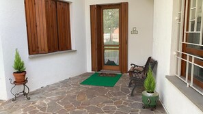 A stone-paved entrance with a wooden door, a bench, and two potted plants. - B&B Chic (Premariacco)