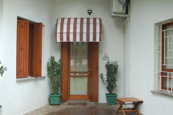 A building entrance with a wooden door, a striped awning, and two potted plants. - B&B Chic (Premariacco)