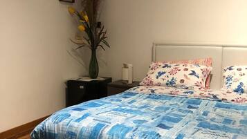 A bedroom with a bed, a nightstand, a vase with flowers, a framed picture, and a painting of a bridge.