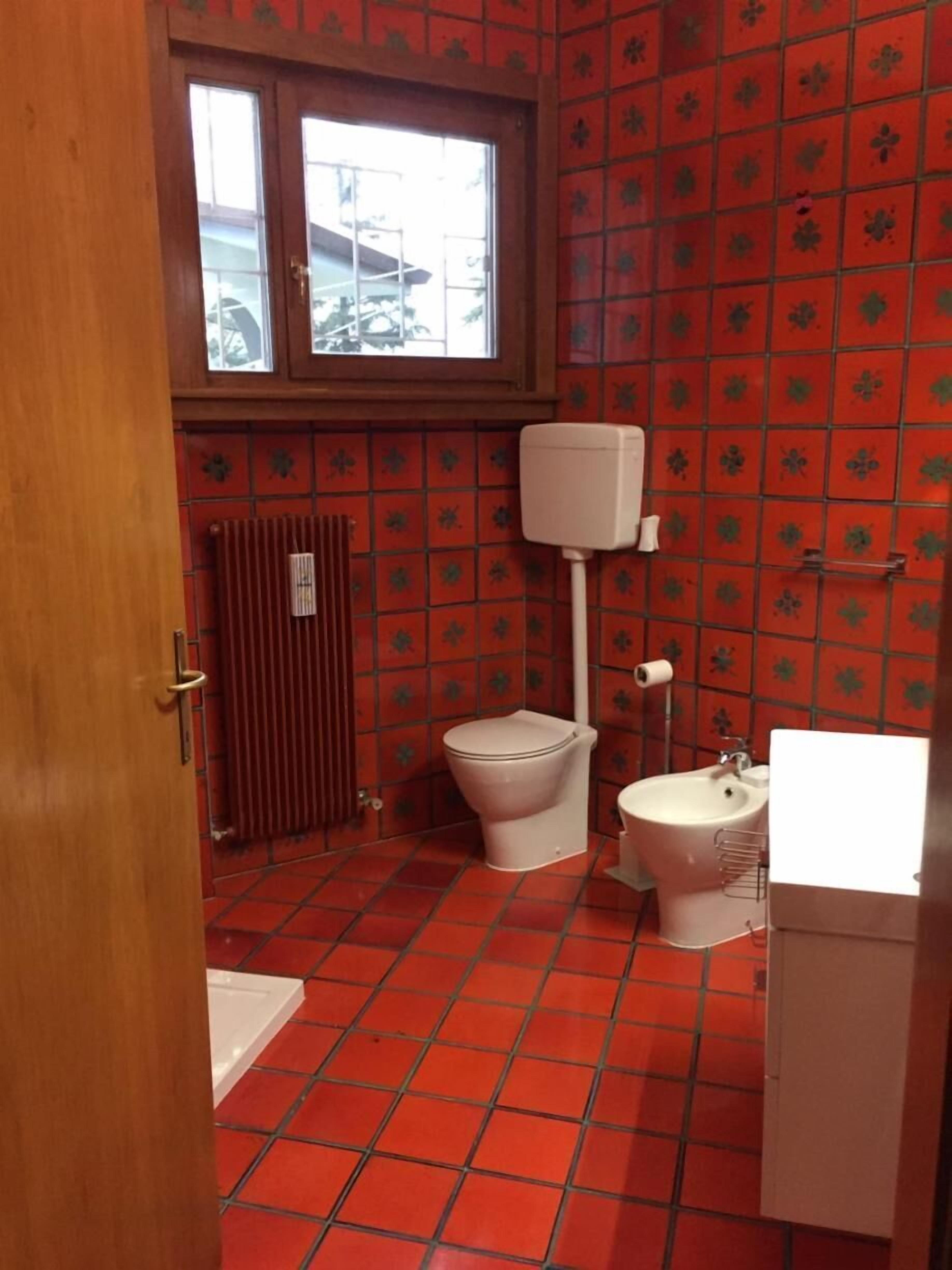 A bathroom with red tiled flooring, a toilet, a bidet, and a radiator.