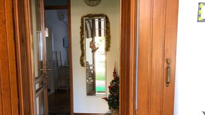 Un pasillo con una puerta de madera, un pequeño árbol de Navidad y una ventana decorada con guirnalda.