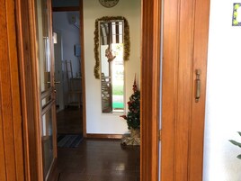 Un pasillo con una puerta de madera, un pequeño árbol de Navidad y una ventana decorada con guirnalda.