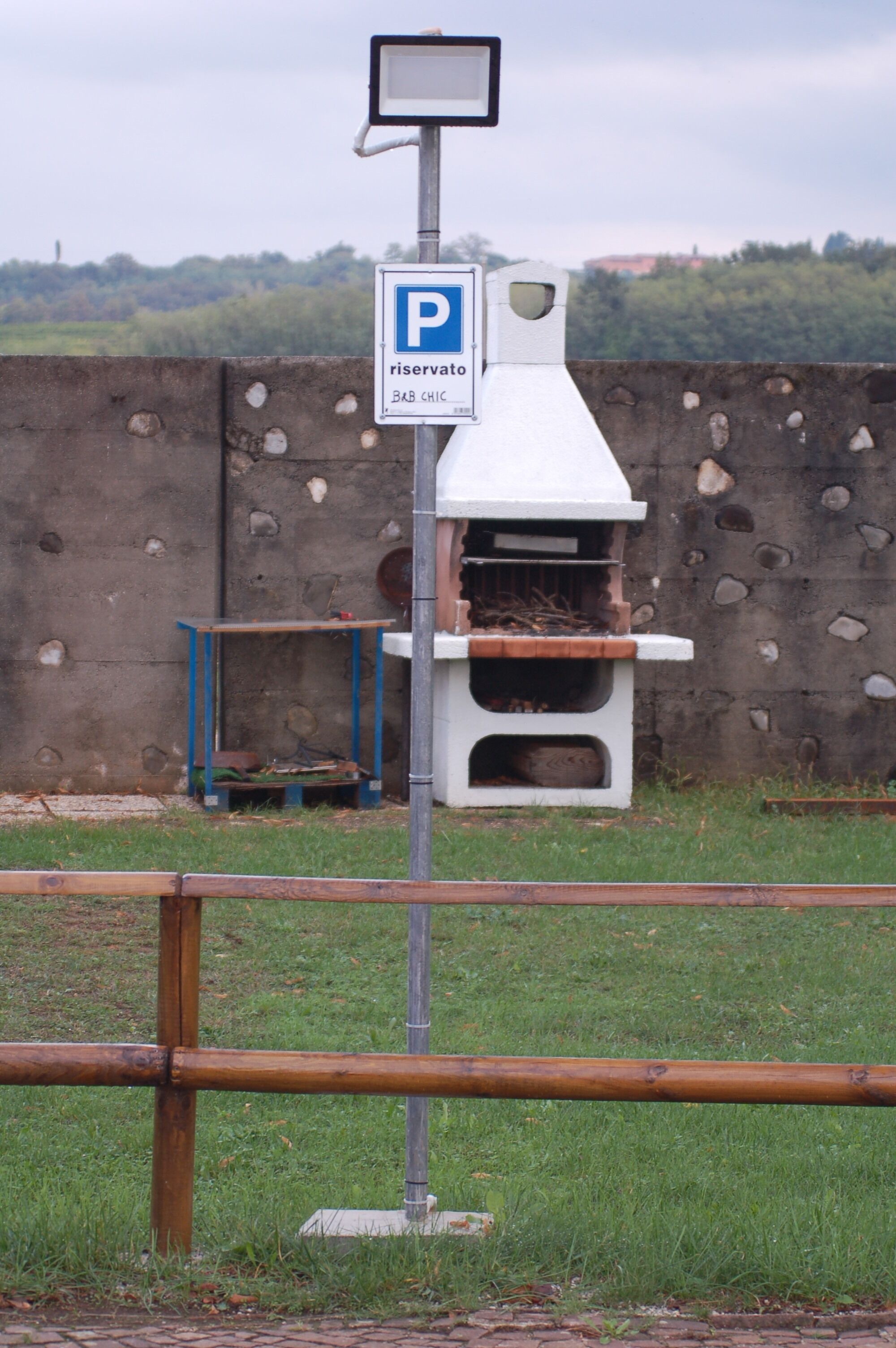 A parking sign with a reservation symbol, a brick oven structure, and a stone wall in the background.