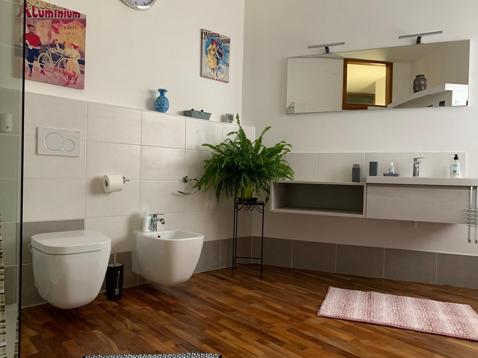 A modern bathroom with a toilet, bidet, sink, and mirror.