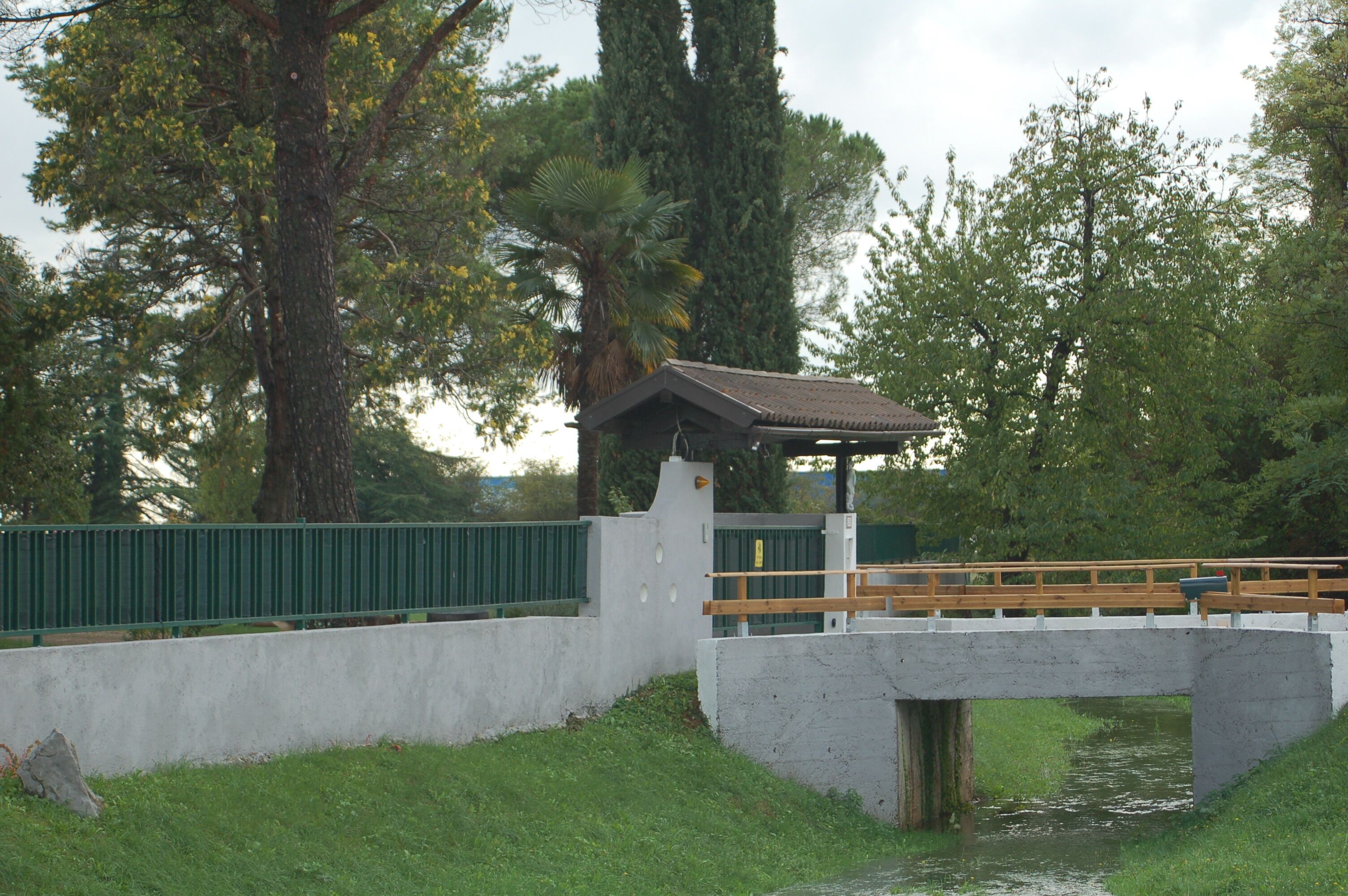 Un ponte in cemento con un piccolo riparo, immerso nel verde e circondato da alberi.