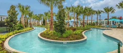 A swimming pool with a curved design, surrounded by palm trees and a covered area with a blue roof.