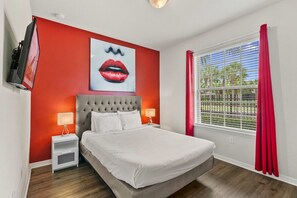 A bedroom with a bed, nightstands, a television, a window with curtains, and a wall with a red accent and a painting. - Disney near 5BR Pool Townhome w Theme Rooms (Kissimmee)