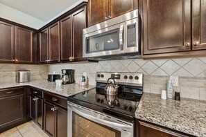 A kitchen with dark wood cabinets, stainless steel appliances, and a granite countertop. - Disney near 5BR Pool Townhome w Theme Rooms (Kissimmee)