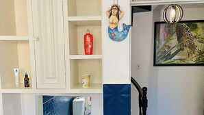 A room with a bed, a nightstand, a dresser, a mirror, a shelf with toiletries, a decorative wall hanging, and a framed picture of a leopard.