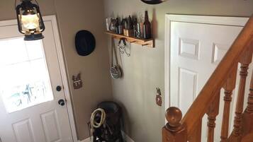 A hallway with a wooden staircase, a lantern hanging from the ceiling, a shelf with bottles and a horn, and a door with a doormat.