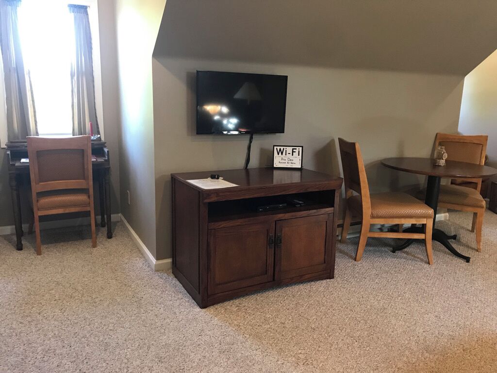 A room with a TV mounted on the wall, a wooden cabinet, two chairs, and a small table.