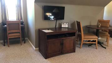 A room with a TV mounted on the wall, a wooden cabinet, two chairs, and a small table.