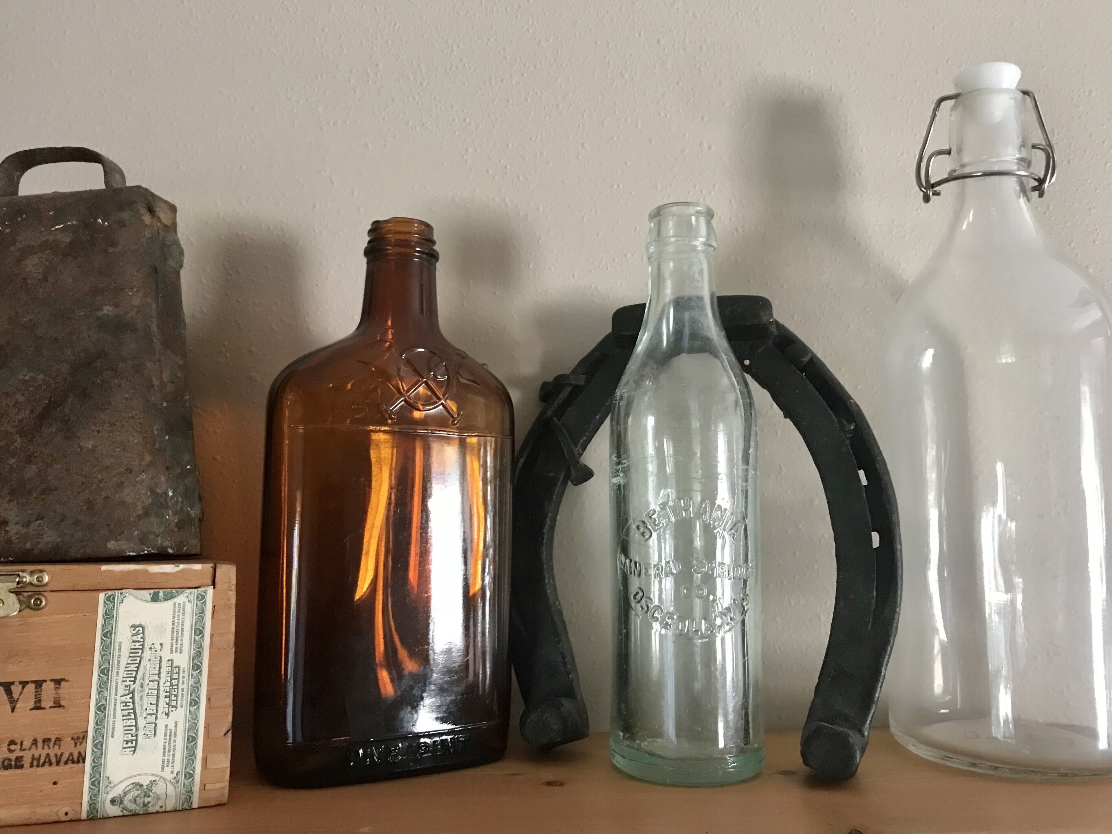 Cuatro botellas de vidrio de diferentes formas y tamaños, un recipiente metálico y una caja de madera con etiqueta.