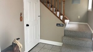 A staircase with wooden railings and a carpeted landing. A sign on the wall reads "Please remove boots & guns."