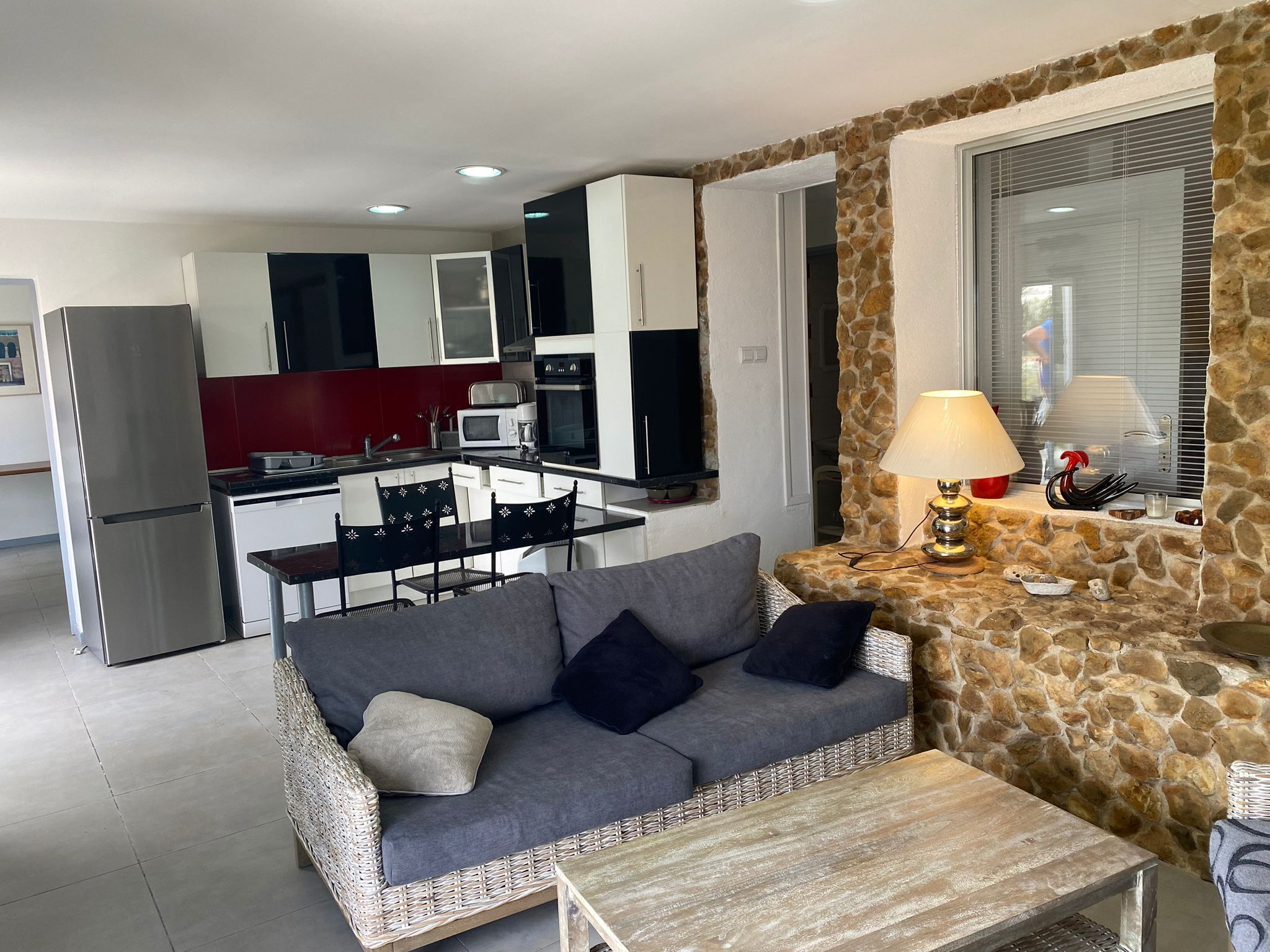 Un espace de vie compact comprenant un coin cuisine, un canapé, une table à manger et un mur décoratif en pierre.