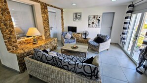 Uma sala de estar com paredes de pedra, móveis de vime e um ventilador.
