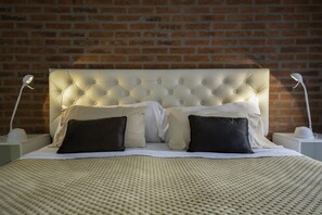 Uma cama bem arrumada com cabeceira estofada, duas luminárias de apoio e uma parede de tijolos ao fundo.
