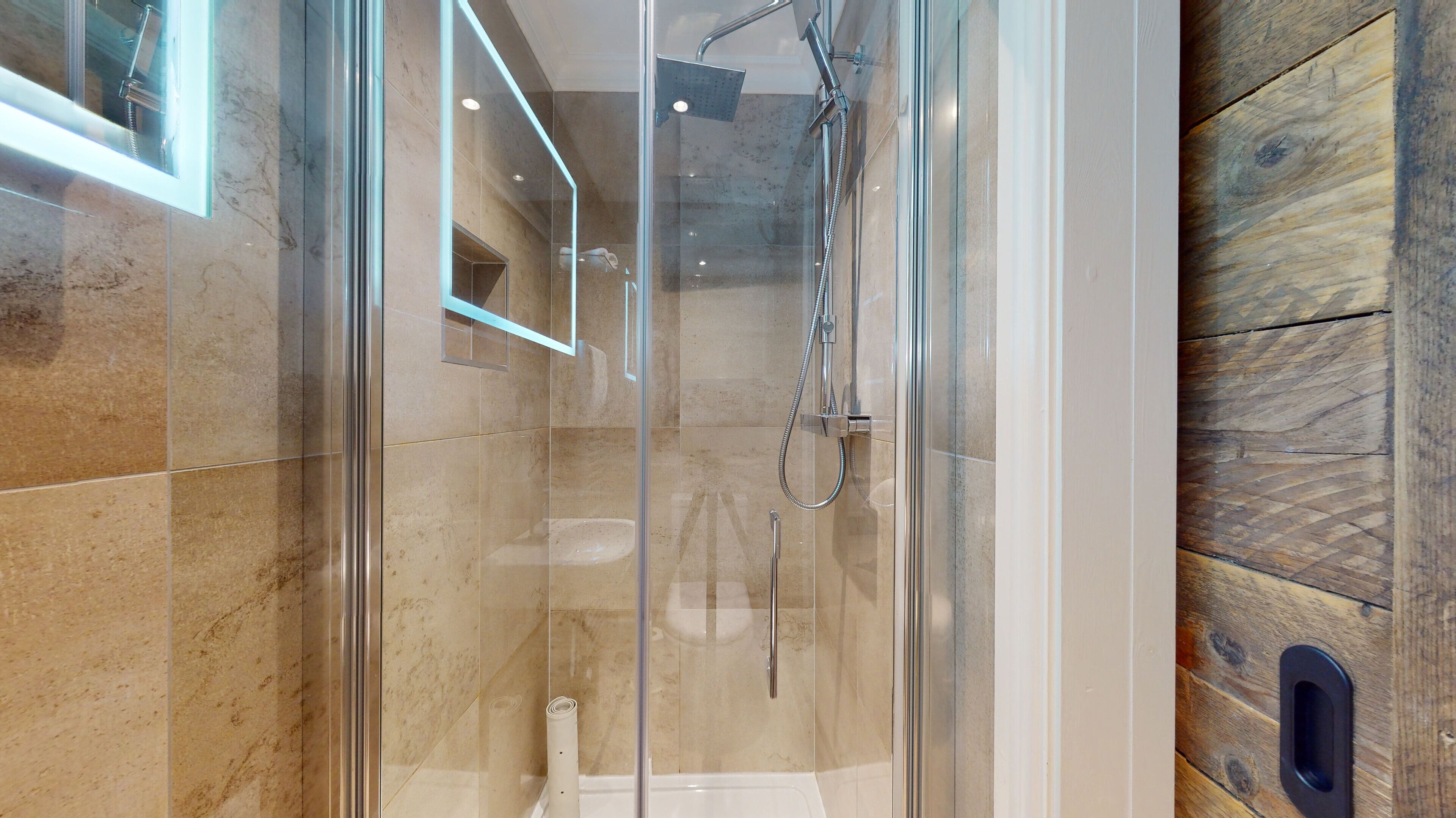 Une douche moderne dotée d’une porte en verre, d’un pommeau de douche à main et d’un robinet mural.