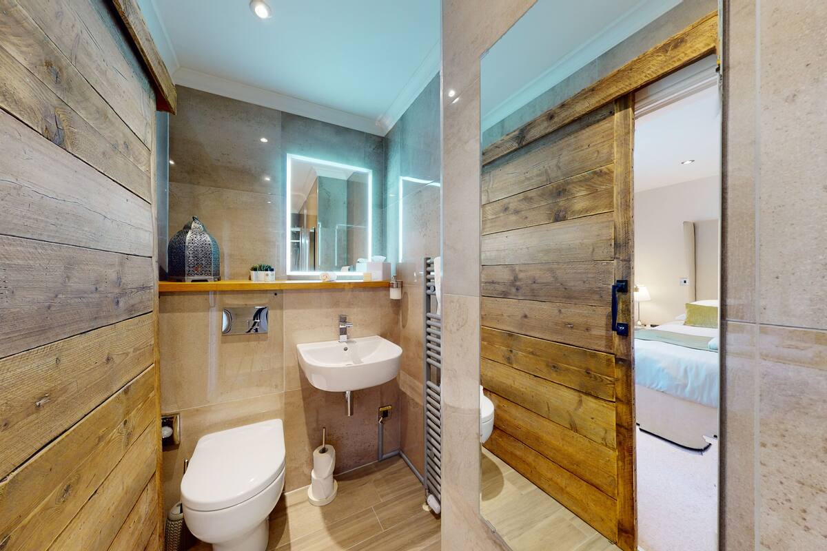 A compact bathroom with a wooden wall, a white sink, a toilet, and a mirror.