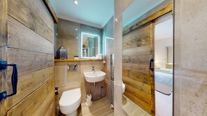 A compact bathroom with a wooden wall, a white sink, a toilet, and a mirror.