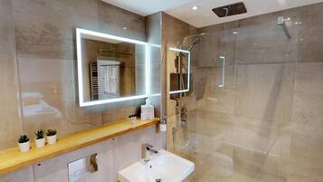 A modern bathroom with a glass-enclosed shower, a large mirror with integrated lighting, a wooden vanity, and a white sink.