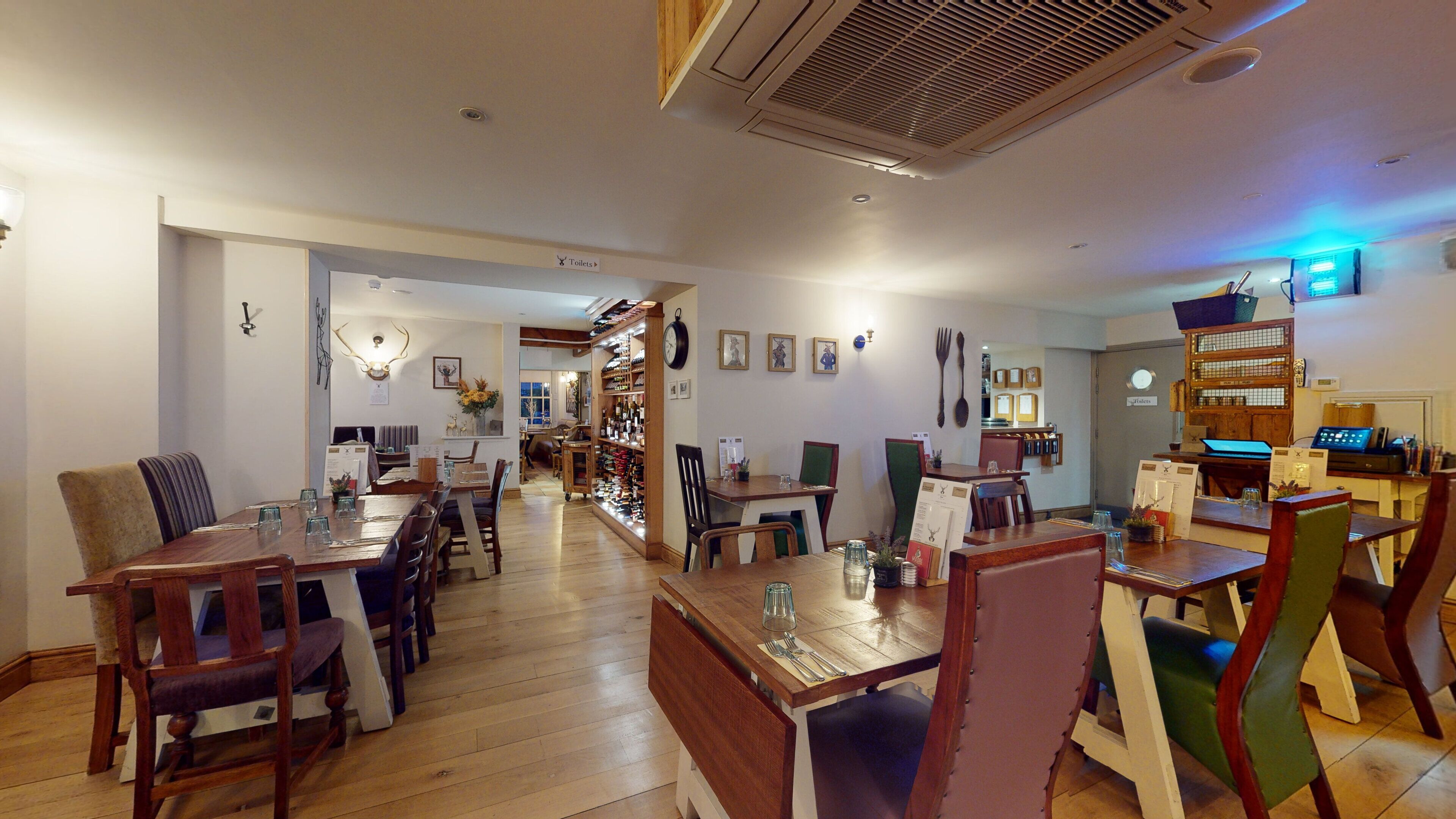 A restaurant with wooden tables and chairs, a bar area, and a display of bottles.