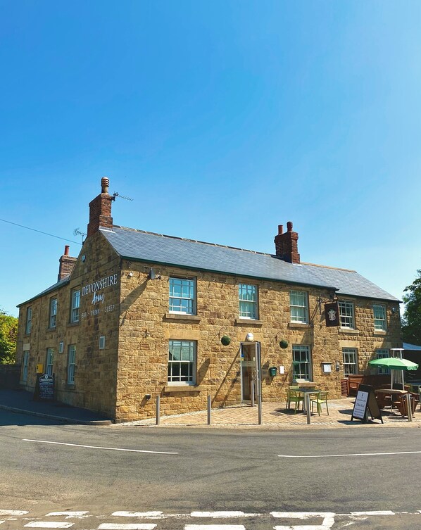 A stone building with a sign reading "Devonshire Arms" and a signboard for "Thrasher's".