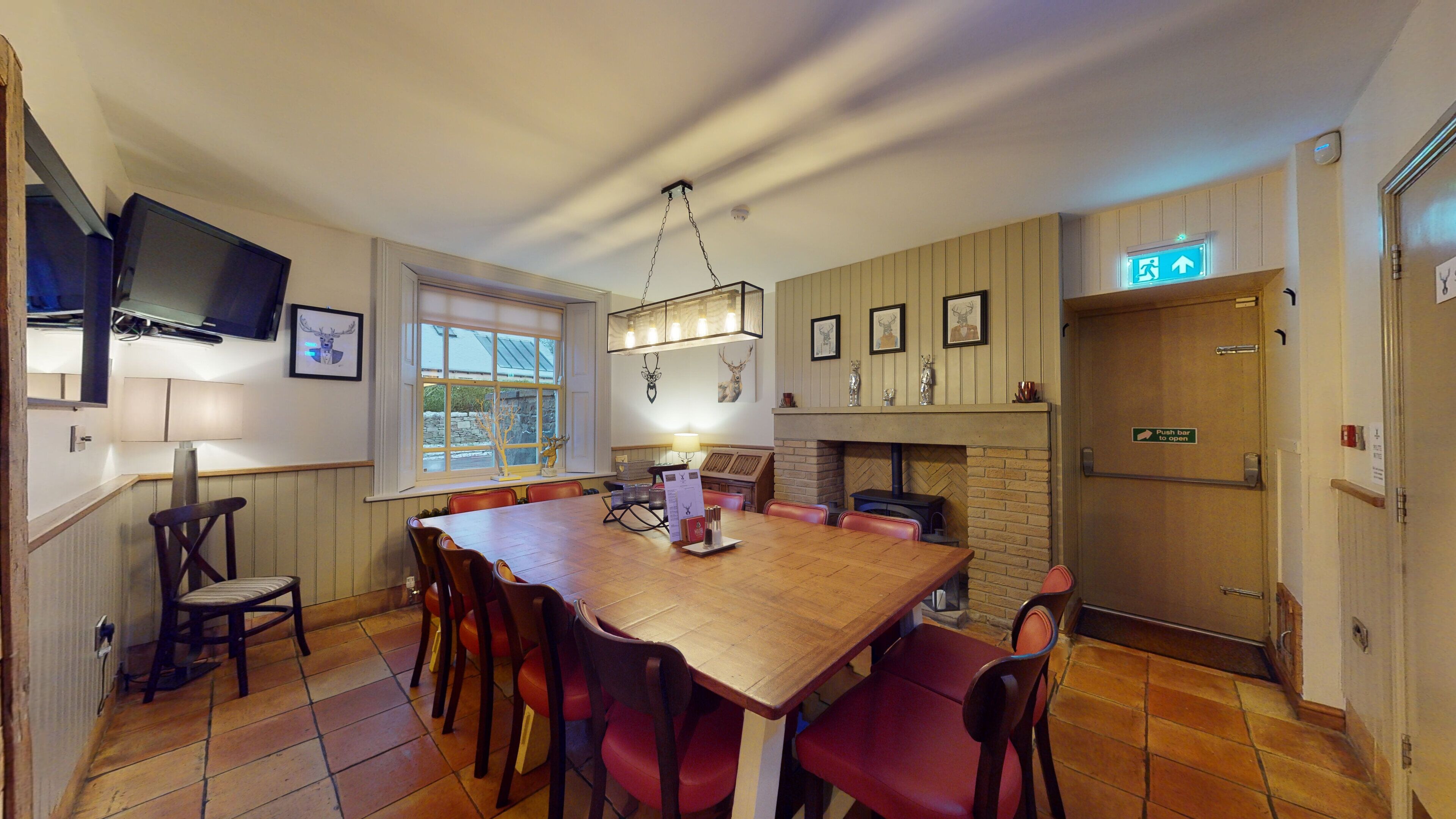 A dining area with a wooden table and red chairs, a fireplace, and a television mounted on the wall.