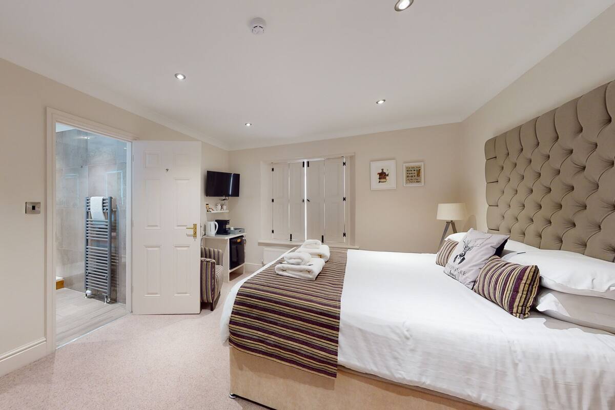 A modern hotel room with a large bed, a flat-screen TV, a desk with a chair, a wardrobe, and a mirror.
