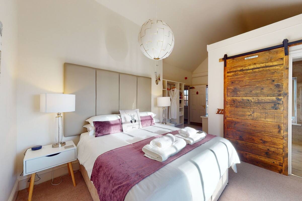 A modern hotel room with a large bed, a desk, a wardrobe, and a sliding door to the bathroom.