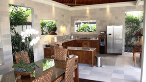A modern kitchen with a central island, built-in appliances, and a dining area with wicker furniture. - Villa Dayak Bali, a luxury tropical resort in the heart of Seminyak (Seminayk)