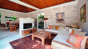 A spacious living area with a wooden ceiling, a fireplace, a television, and a sofa with cushions. - Villa Dayak Bali, a luxury tropical resort in the heart of Seminyak (Seminayk)