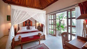A bedroom with a wooden canopy bed, a large window with a view of greenery, and a wooden desk with a lamp. - Villa Dayak Bali, a luxury tropical resort in the heart of Seminyak (Seminayk)