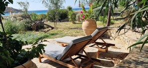A sunlit outdoor seating area with two wooden lounge chairs and a large terracotta pot with flowers.