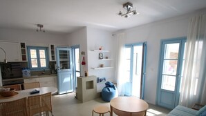 A modern, well-lit living room with a dining area, kitchen, and a large window with curtains. - Beautiful beachfront property (Chora, Ios)