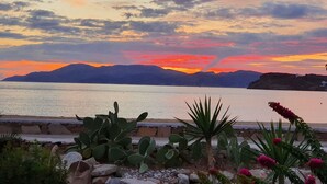 A coastal landscape with a sunset, mountains in the background, and desert plants in the foreground. - Beautiful beachfront property (Chora, Ios)