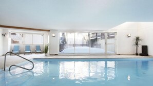 An indoor swimming pool with clear glass walls, blue chairs, and a view of a snowy outdoor area. - 300m from ski slopes, swimming pool, balcony, tv, ski locker, 28m², Notre Dame de Bellecombe (Notre-Dame-de-Bellecombe)