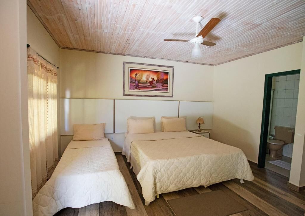 Een slaapkamer met twee bedden, een plafondventilator, een schilderij en een zichtbare badkamer door een open deur.