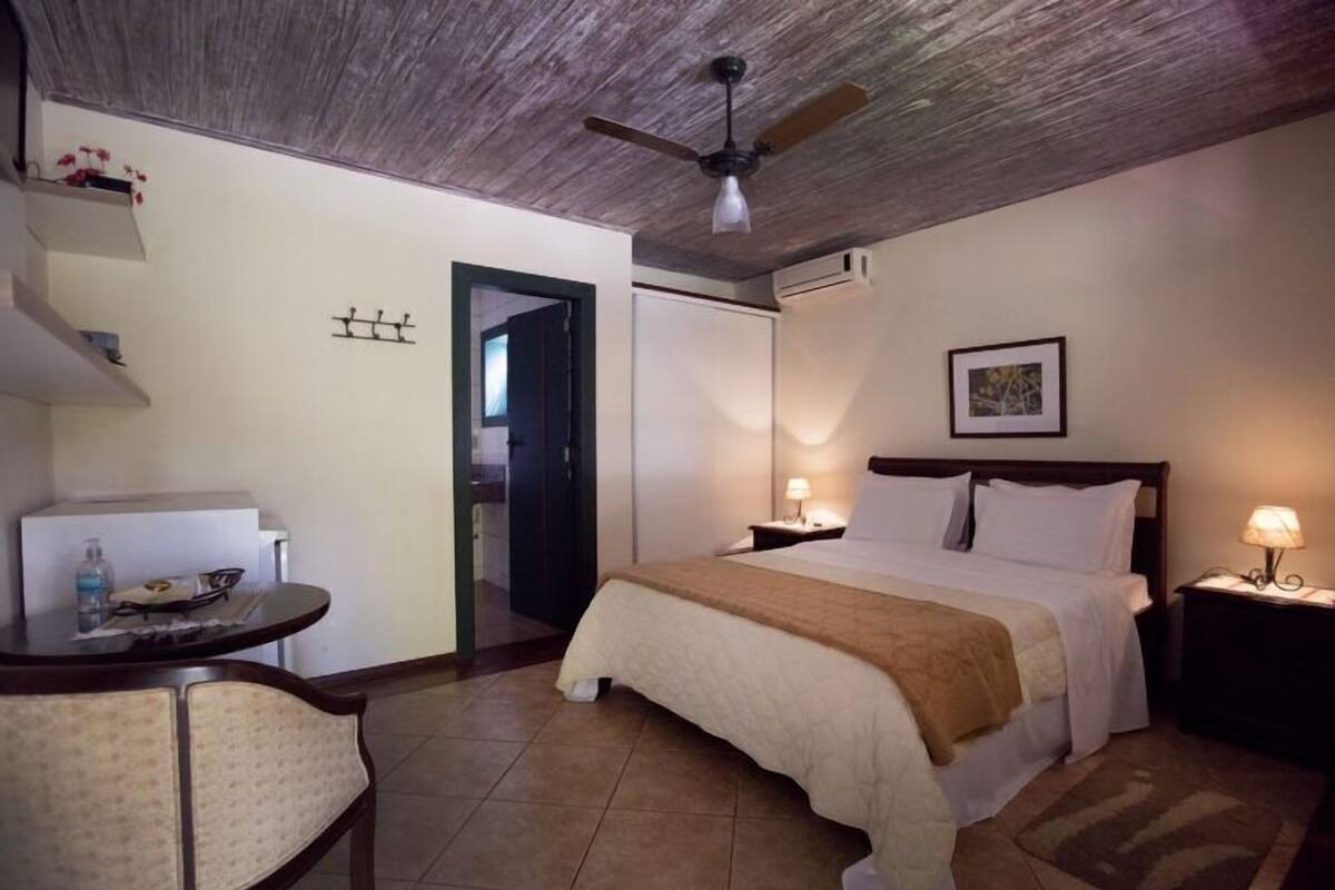 Una habitación de hotel con cama, mesitas de noche, una silla, escritorio y ventilador de techo.