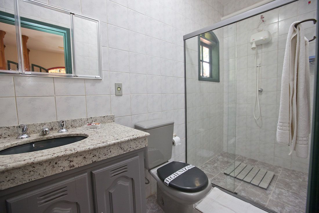 Un baño con lavamanos de encimera de granito, inodoro con tapa, mampara de cristal en la ducha y una toalla colgada en un perchero.