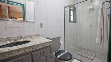 Un baño con lavamanos de encimera de granito, inodoro con tapa, mampara de cristal en la ducha y una toalla colgada en un perchero.