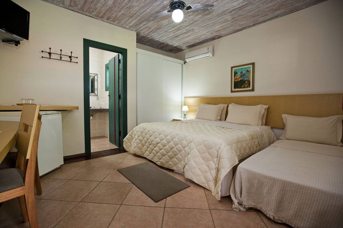 Un dormitorio con dos camas, un escritorio, una silla, un refrigerador pequeño y una puerta que da a otra habitación.