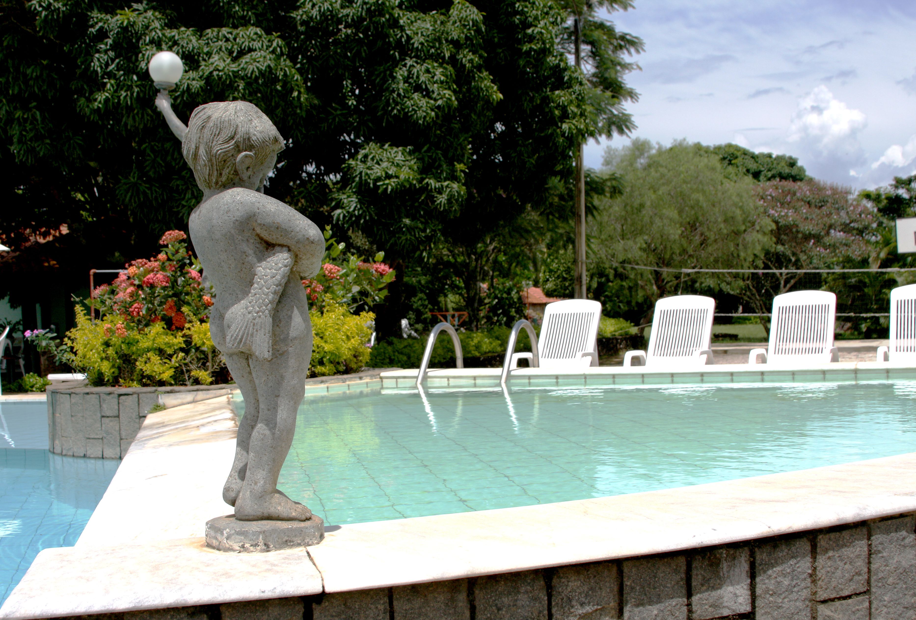 A stone statue of a figure holding a ball by a poolside.