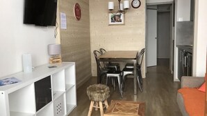 A modern living room with a TV, wooden wall paneling, a dining area with chairs and a table, and a kitchen area with a stove. - Ski-in/ski-out & foot of the slopes, 4th floor, view mountain, balcony, tv, ski locker, 23m² (La Plagne)
