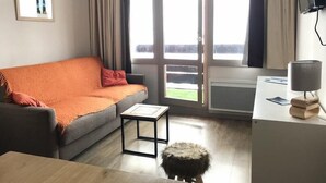 A modern living room with a grey sofa, a small wooden table, a fluffy stool, and a desk with a lamp. - Ski-in/ski-out & foot of the slopes, 4th floor, view mountain, balcony, tv, ski locker, 23m² (La Plagne)